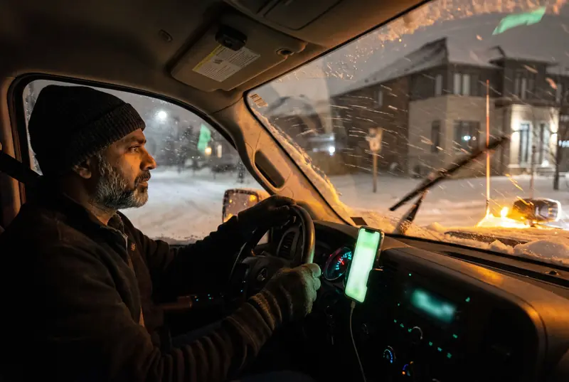 A plow driver at night with a phone in a dashboard mount showing an incoming call