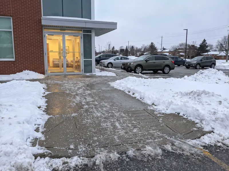 A cleared and salted walkway and ramp at the entrance of a small medical building after a storm